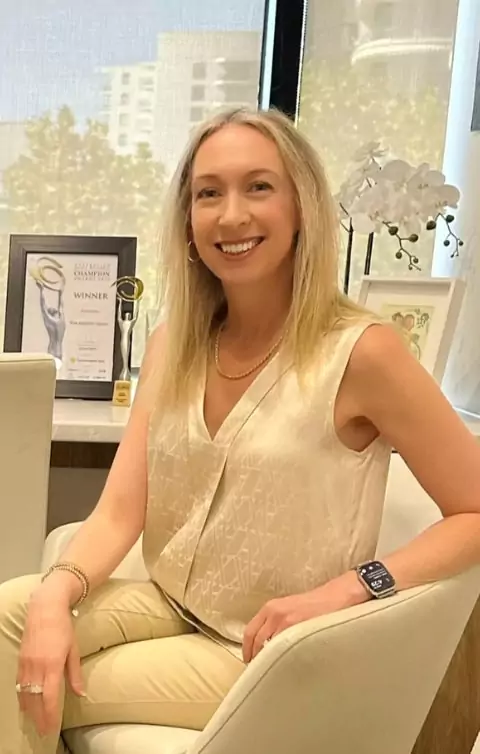 Dr Jodie Lowinger smiling in her office, seated beside an award, representing her leadership coaching and high-performance workshops.